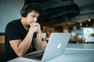 A man wearing headphones sits looking at a laptop screen